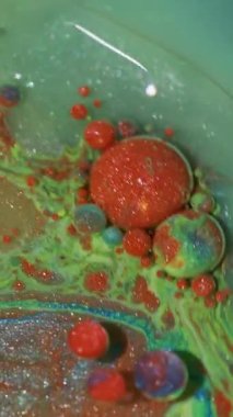 Dikey video. Yağ dokusu. Mürekkep döküldü. Odaklanmamış kırmızı mavi renkli parlak turuncu su kabarcıkları soyut arkaplanda yüzüyor..