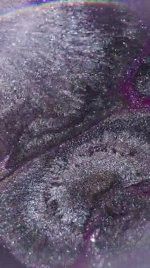 Dikey video. Boya sıçraması. Odaklanmamış çember akışı. Bulanık mor gümüş rengi parlak desen soyut koyu siyah arkaplanda yayılan parçacıklar..