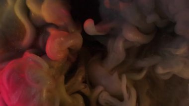 Akrilik mürekkep dumanı. Soyut sim sisi. Odaklanmamış turuncu pembe renkli bulut parçacıkları gökkuşağı resimleri koyu siyah arka planda yayılıyor..