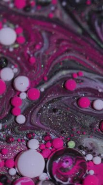 Dikey video. Petrol dökülüyor. Akrilik boyalı su. Bulanık pembe mor renk soyut arkaplanda yüzen parlak lekeler..