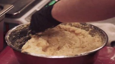 Mutfak süreci. El yapımı hamur işi. Eldivenli fırıncı, profesyonel mutfakta elektronik pulların yanındaki metal kasede hamur malzemelerini karıştırıyor..