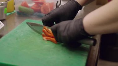 Yemek hazırlama. Dolmalık biber kesiyorum. Şefin eli eldivenle mutfak tahtasındaki kırmızı çiğ sebze dilimlerini sağlıklı yemek için kesiyor..