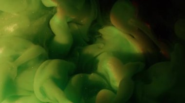 Su altı boya bulutu. Parlak gökkuşağı mürekkebi. Odaklanamayan yeşil renk, parlak su dokusunu soyut siyah sanat arka planına yayıyor..
