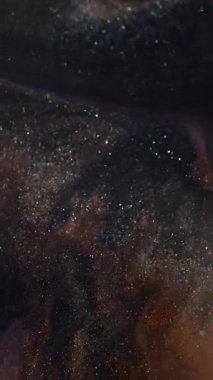 Dikey video. Işıltılı bokeh. Bulanık boya dokusu. Odaklanmamış altın rengi pembe su pulları soyut koyu siyah arkaplanda sıvı akışı sağlar.