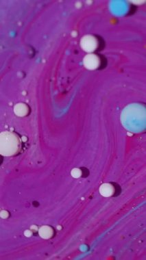 Dikey video. Mürekkep parçacıkları. Suyu boya. Odaklanmamış pembe renkli damlacıklar soyut sanat arka planında yüzen yağ beyaz mor sıvıyı parlatırlar..