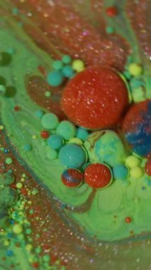 Dikey video. Mürekkep parçacıkları. Suyu boya. Odaklanmamış yeşil mavi parlak yağ sarı turuncu damlacıklar soyut arkaplanda ışıldayan sıvılar