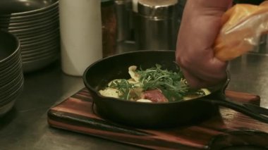 Tabak hazırlanıyor. Mutfak süreci. Şef, akşam yemeğine roka sosu ekliyor. Kızartma tavasında yeşil yapraklı iştah açıcı sıcak yemek..