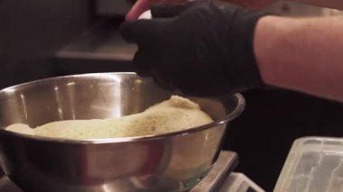 Yemek pişirmek. Hamur hazırlıyorum. Şefin elleri eldivenli, metal kasede yumurta kırıyor. Üzerinde un var. Profesyonel mutfak kontrolü..