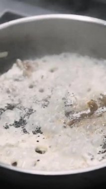 Dikey video. Yahni sosu. Baharatlı sıcak yemek. Şefin eli kaynamış beyaz sıvıda eti tavaya koymak için karabiber tuzu ekliyor. Ocakta kaynayan buharlı yemekler..