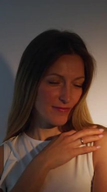 Dikey video. Kendine güvenen bir kadın. Pozitif ruh hali. Memnun, sakin kadın, hafif gölge ellerle yüzlere dokunmaktan hoşlanıyor..