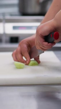 Dikey video. Salatalık dilimliyorum. Sebze doğrama. Şef, vejetaryen yemeği için beyaz tahta üzerinde bıçak doğruyor. Taze ve sağlıklı yiyecekler..