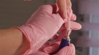 Dikey video. Çivi prosedürü. Salon tedavisi. Eldivenli kadın manikürcü elleri değirmenci kadın bakımıyla müşteri parmağını kesiyor..