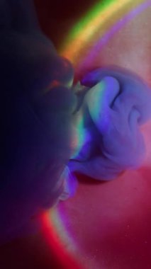 Dikey video. Parıltı karışımı. Parlak sıvı. Siyah arka planda yayılan pembe mavi menekşe ışıltısı. Renkli gökkuşağı hafif kemer mürekkebi soyut karışım bulanık su.