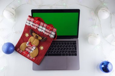 Yeşil ekranlı bir dizüstü bilgisayar, Noel süslemeleri olan beyaz bir masada.