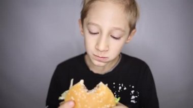 Çocuk kamera önünde hamburger yiyor.