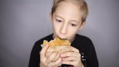 Çocuk kamerada hamburger yiyor.