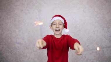 Kırmızı Noel Baba şapkalı ve maytaplı bir çocuk mutlu yıllar diler.