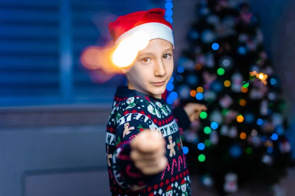 Chłopiec Kapeluszu Świętego Mikołaja Iskierkami Dłoniach Tle Choinki Neonowym Światłem — Zdjęcie stockowe