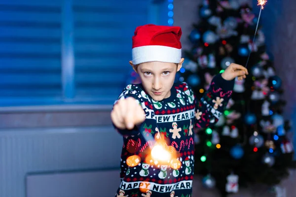 Chłopiec Kapeluszu Świętego Mikołaja Iskierkami Dłoniach Tle Choinki Neonowym Światłem — Zdjęcie stockowe