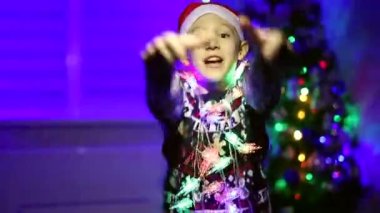 Noel Baba şapkalı bir çocuk yeni yıl arkaplanda çelenklerle dans ediyor.