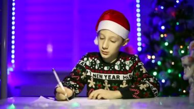 Noel ağacının arka planında bir çocuk Noel Baba 'ya mektup yazıyor.