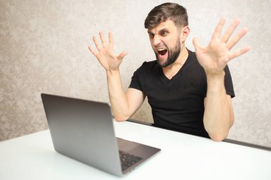 Sakallı bir adam sürpriz bir şekilde dizüstü bilgisayar üzerinde çalışıyor.