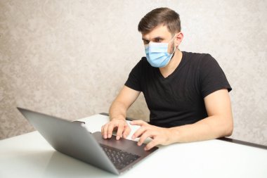 Tıbbi maskeli bir adam bilgisayarda çalışıyor.