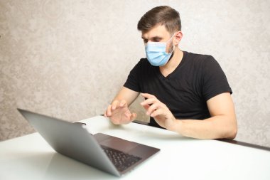 Tıbbi maskeli bir adam bilgisayarda çalışıyor.