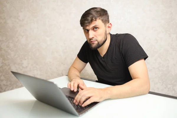 a man is typing on a laptop and looking at the camera