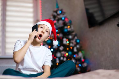 Noel Baba şapkalı bir çocuk telefonda çelenk takmış konuşuyor.