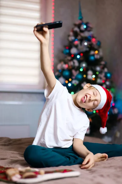 サンタクロースのクリスマスの帽子の子供はクリスマスツリーの背景で幸せです — ストック写真
