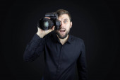 Muž fotograf v černé košili se dívá hledáčkem kamery