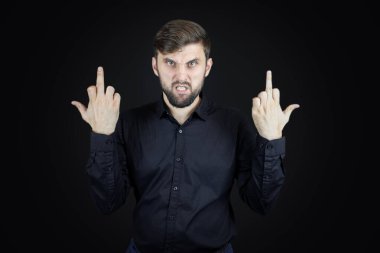 Siyah gömlekli ve siyah arka planlı bir adam orta parmaklarının müstehcen hareketler yaptığını gösteriyor.