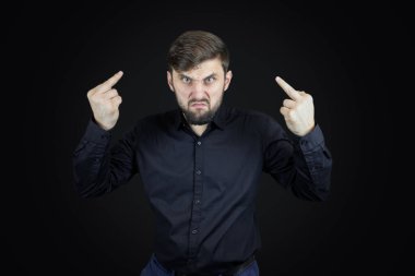 Siyah gömlekli ve siyah arka planlı bir adam orta parmaklarının müstehcen hareketler yaptığını gösteriyor.