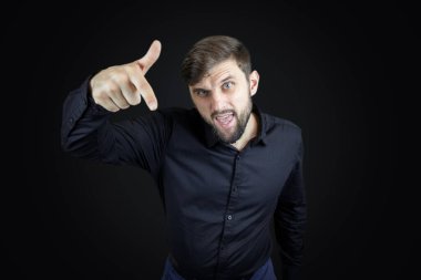 Siyah gömlekli ve siyah arka planlı bir adam işaret parmağını aşağı doğru gösteriyor.