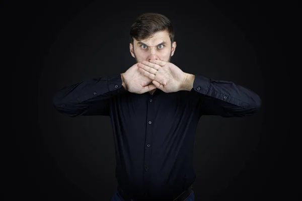 a man in a black shirt and on a black background covered his mouth with his hands