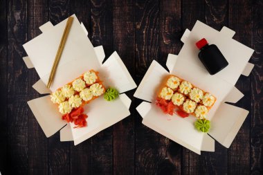 Suşi ruloları ve peynirle ahşap bir masada açık bir kağıt kutunun içinde.