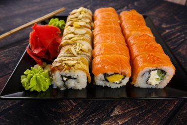 Siyah tabakta wasabi peyniri, zencefil ve somon soslu suşi.