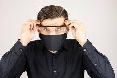 Siyah koruyucu maskeli bir adam ellerini tıbbi gözlüklerinin arkasına koydu.