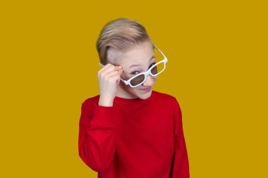 Kırmızı elbiseli ve gözlüklü havalı çocuk sarı arka planda şaşkınlık duyguları gösteriyor.