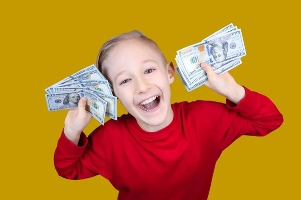 一个穿着红色衣服的快乐的孩子在他面前拿着一堆美元的钞票 — 图库照片
