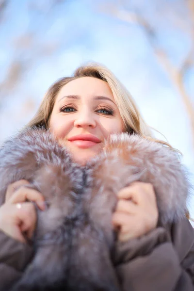 a beautiful blonde in a jacket with a fur collar looks down from above