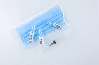 Tıbbi maskenin yanında COVID 19 aşısı ve enjeksiyon için bir şırınga var.