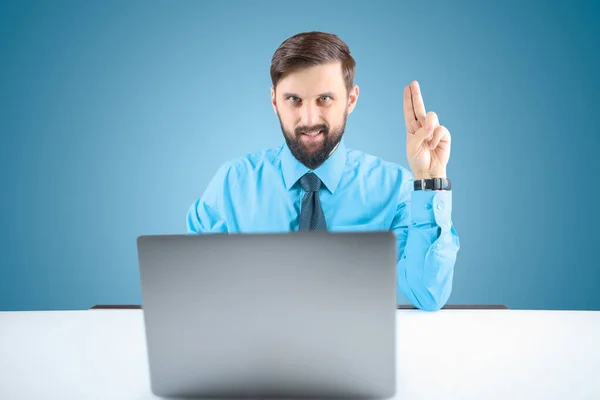 青いシャツを着たビジネスマンが手を挙げて2本の指を見せますコンピュータのオフィスで髭を生やした男です ストックフォト