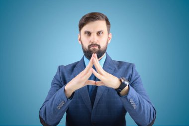 Takım elbiseli adam parmaklarını birleştiriyor, iş adamı odaklanıyor ve dümdüz bakıyor.