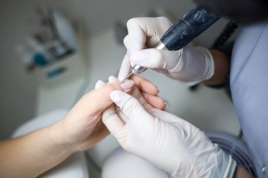 Manikür ustası, manikür makinesini müşterinin elinde tutar ve her çiviyi verniğe hazırlar.