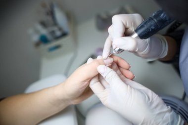 Manikür ustası, manikür makinesini müşterinin elinde tutar ve her çiviyi verniğe hazırlar.