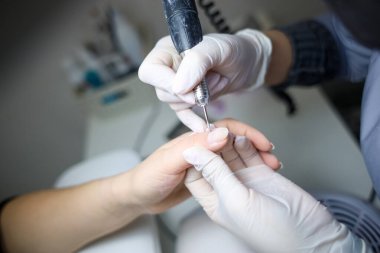 Manikür ustası, manikür makinesini müşterinin elinde tutar ve her çiviyi verniğe hazırlar.