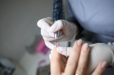 Manikür ustası, manikür makinesini müşterinin elinde tutar ve her çiviyi verniğe hazırlar.