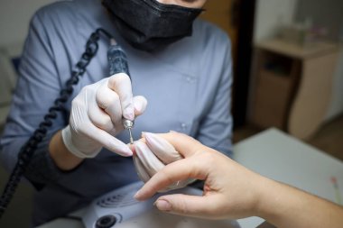Güzellik salonundaki manikür ustası donanım manikürü yapıyor, müşterinin parmaklarındaki tırnak etlerini tedavi ediyor.